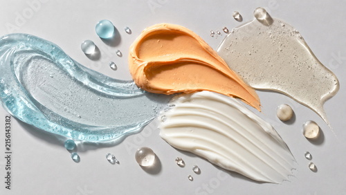 Elegant skincare texture arrangement featuring translucent blue gel, peach cream, white moisturizer and clear serum on a cool neutral background.