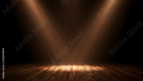 A dimly lit indoor stage with polished wooden flooring illuminated by bright overhead spotlights casting strong beams and dust particles floating in the warm atmospheric air against deep shadows