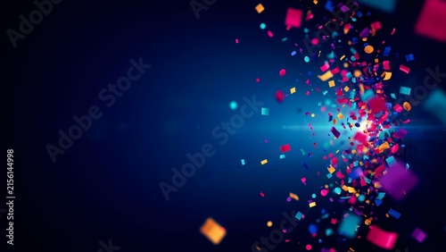 An explosive burst of multicolored confetti and shiny metallic particles scatters across a dark blue background with bright glowing light rays and celebratory festive motion blur effects