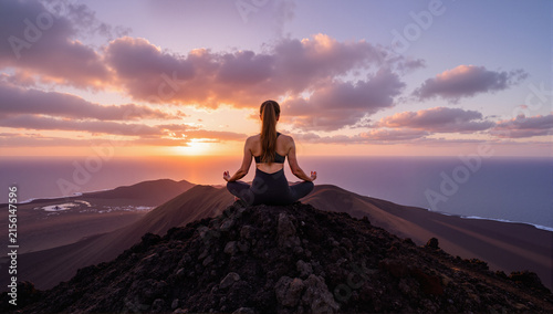 Girl doing yoga lotus position on the top of a volcano at sunset in Fuerteventura, Canary Islands
