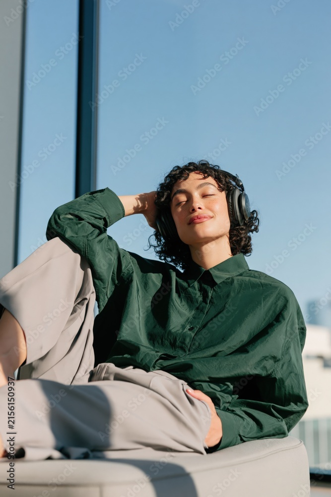 Obraz premium Person relaxing with headphones seated in sunlit modern lounge wearing a green shirt for relaxation and lifestyle background and banner design