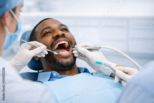 Dental professional examining an adult patient's teeth with a mirror and suction tool during a chairside oral checkup.