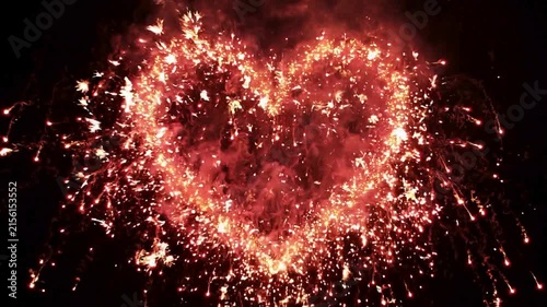 Heart shape made of sparkling red firework sparks glowing brightly on a dark night.