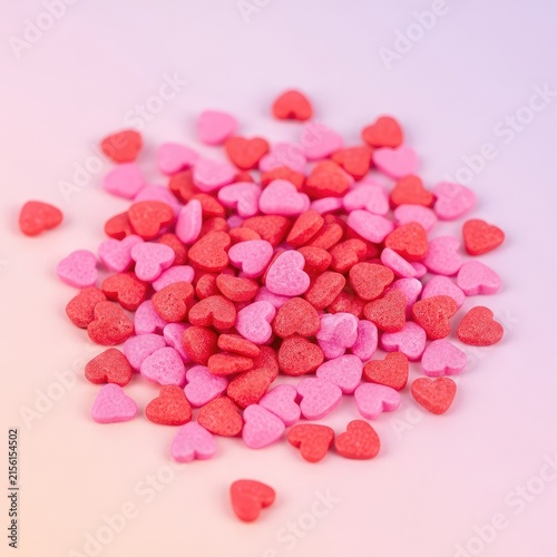 Vivid pink and red heart-shaped sugar sprinkles scattered over a soft pastel background, creating a festive texture for pastry decoration, sweet, macro, romantic