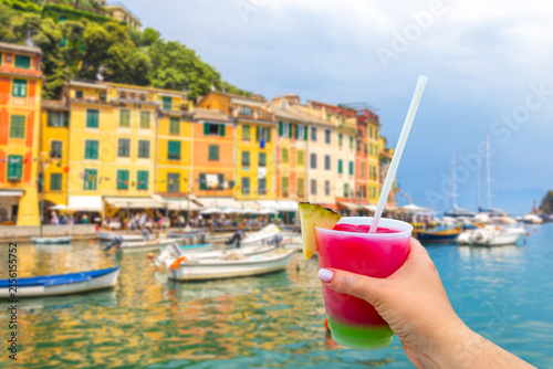 Foto Portofino with colorful houses and villas in little bay harbor with hand holding a glass with cocktail and straw