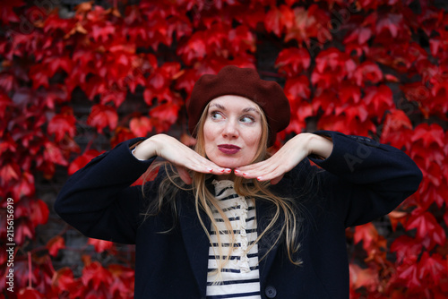 Fashionable woman in warm fall outfit posing against bright red autumn leaves, seasonal lifestyle concept.