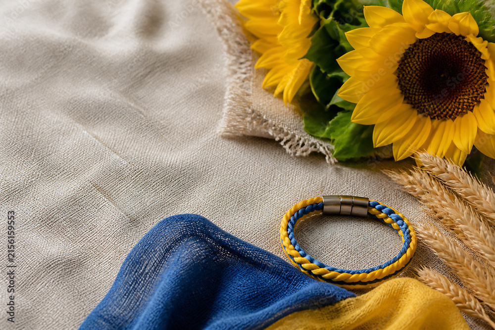 Fototapeta premium A close-up of a light fabric surface with sunflowers, a blue and yellow bracelet, and some dried wheat stalks.