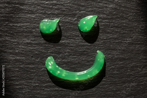 Green gel toothpaste arranged into smiling face shape on dark slate surface