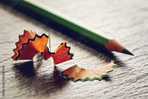 Sharpened green pencil with wooden shavings resting on dark textured slate background