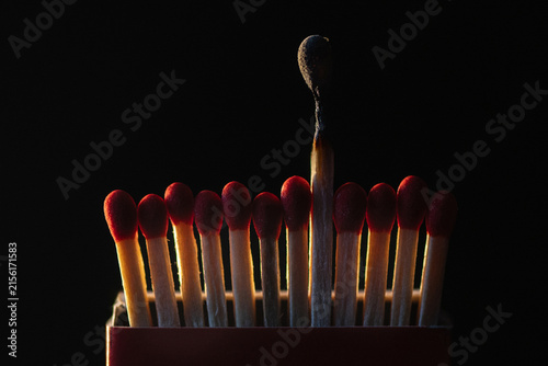 Single burned matchstick standing taller than unused red matches in box
