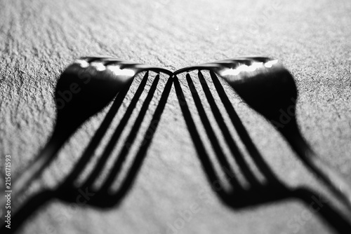 Two silver forks touching tips with shadows on dark textured slate background