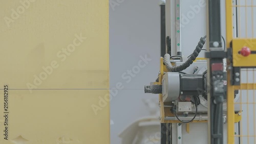 A close-up of a large polyurethane foam block being cut on a CNC machine. Automated CNC foam cutting machine processing a large block of polyurethane foam in a modern factory setting.