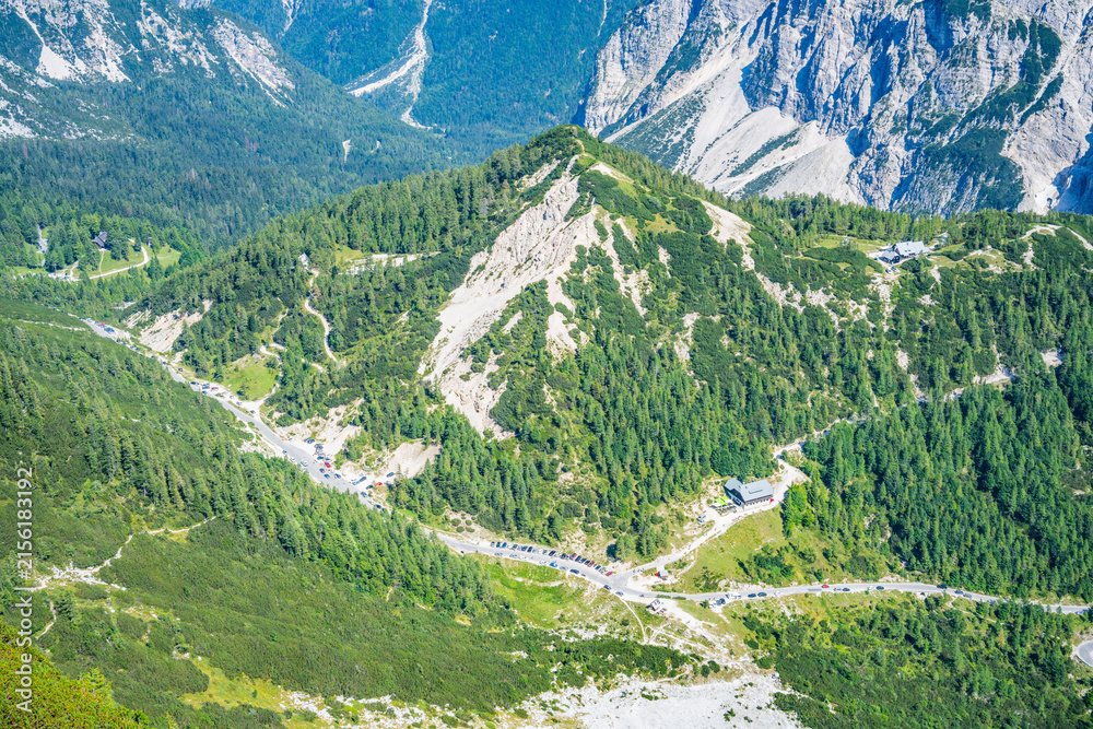 Fototapeta premium Vrsic Pass shows a winding road through green forests and rocky mountains in Slovenia. This high road is a start for many hiking paths at a popular outdoor location.