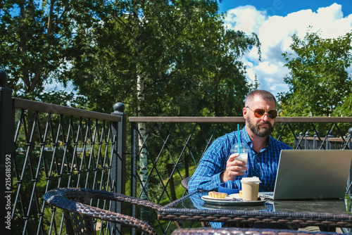 Mature businessman having online video meeting on laptop while working remotely from outdoor cafe terrace in summer