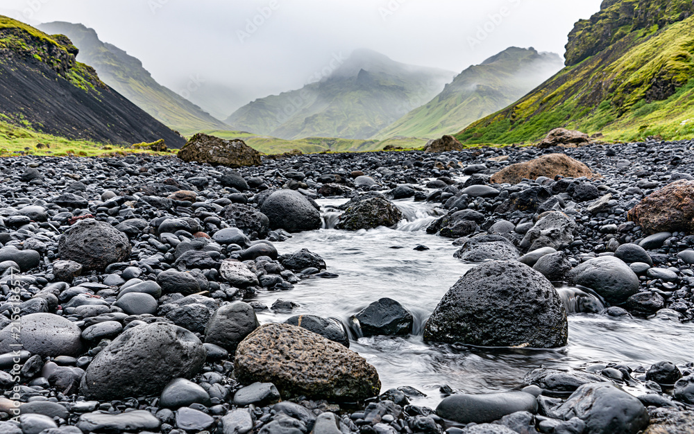Obraz premium Rocky shallow mountain river in Iceland, flows against the backdrop of mountains.