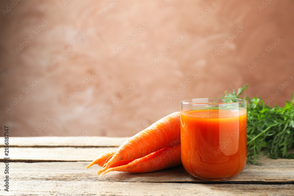 Naklejka premium Fresh carrot juice in glass and ripe vegetables on wooden table, space for text