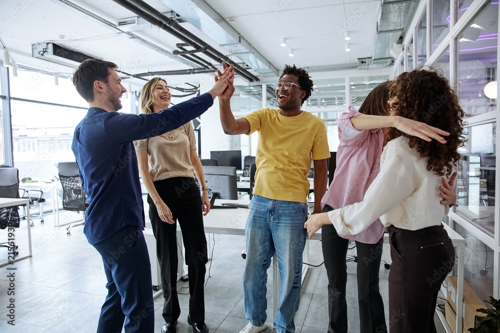 Obraz premium Diverse business team giving high-five during a collaborative office meeting
