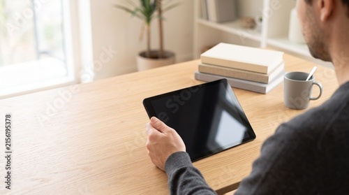 Man holding tablet blank screen mockup for digital content presentation in bright modern home office workspace interior background