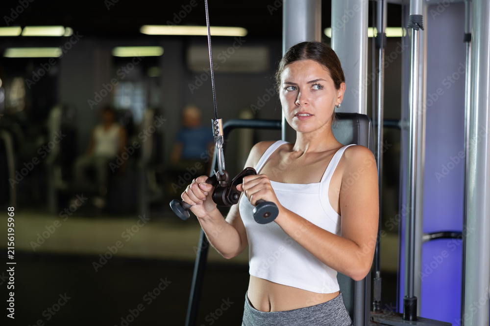 Fototapeta premium Slender athletic girl work out muscles of arms and shoulders on rope loop simulator in gym of fitness club