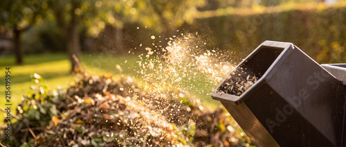 Garden wood chipper machine processing wood into mulch during sunset in a backyard