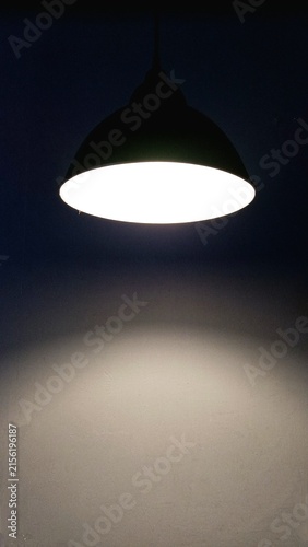 A minimalist black pendant lamp illuminating a textured wall, creating a dramatic contrast between light and shadow in a dark interior setting