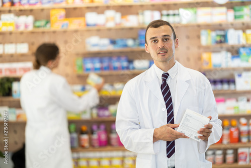 Bild auf Leinwand Kind young apothecary holding a box with remedy standing against shelves full of