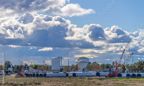 Disassembled giant wind turbine parts, tower segments, and construction cranes at an industrial site under a dramatic cloudy sky, showcasing renewable green energy development and technology