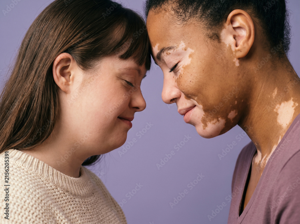 Fototapeta premium Two diverse women touching foreheads against purple background