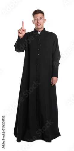 Young priest in cassock pointing upwards on white background