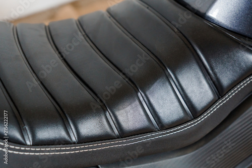 Close up of a black ribbed leather motorcycle seat with white stitching and a modern texture.
