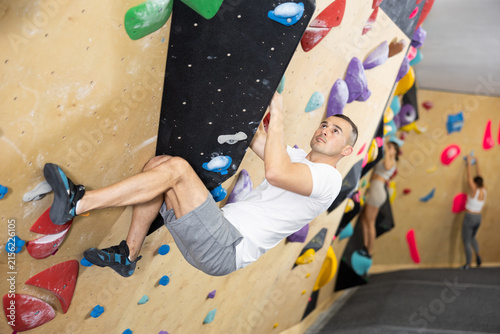 Photography Motivated young man carefully maneuvering without ropes and harnesses on artificial bouldering wall in modern climbing center