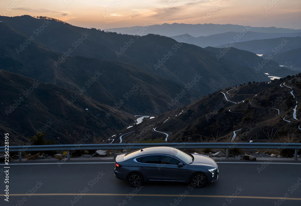 Obraz premium Dark gray sedan driving on a winding mountain road at sunset with a scenic valley view
