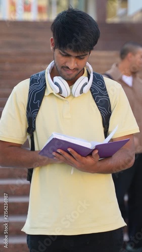 Young indian male student reading book on campus steps
