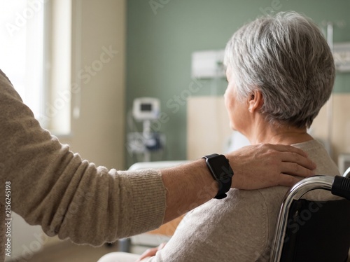 Professional caregiver comforting elderly woman with gentle shoulder touch at home