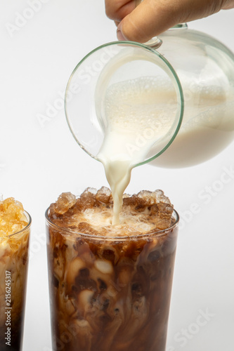Close-up of a hand pouring milk from a jug into cold coffee drinks