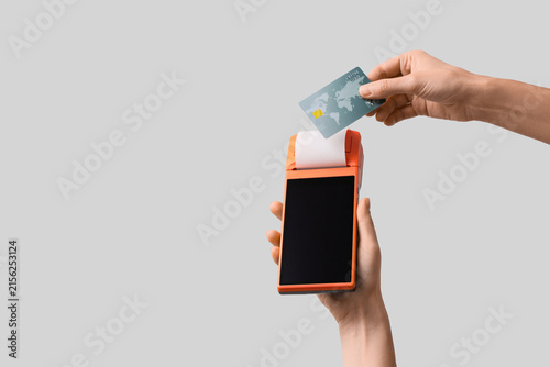 Female hands with payment terminal and credit card on light background