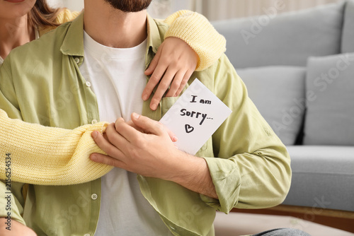 Hugging couple holding paper with text I AM SORRY at home, closeup