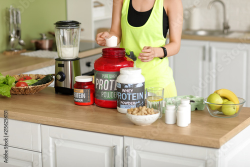 Sporty young woman making protein shake in blender at home, closeup