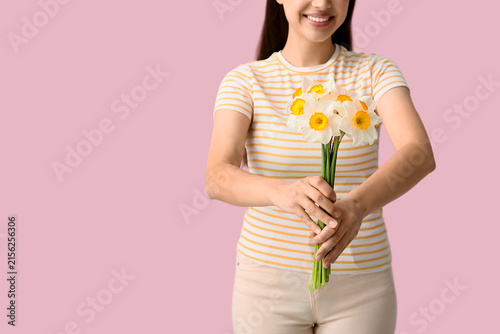 Young woman with bouquet of daffodil flowers on pink background