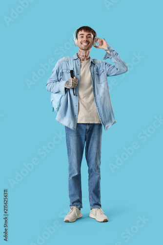 Young tattooed student in headphones listening to music on blue background