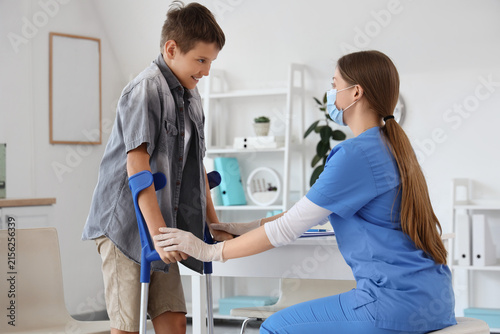 Injured little boy with crutches and doctor in clinic