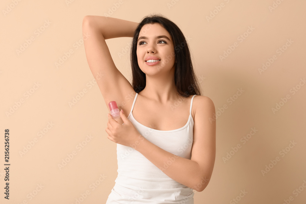 Obraz premium Happy smiling young woman using crystal deodorant on beige background