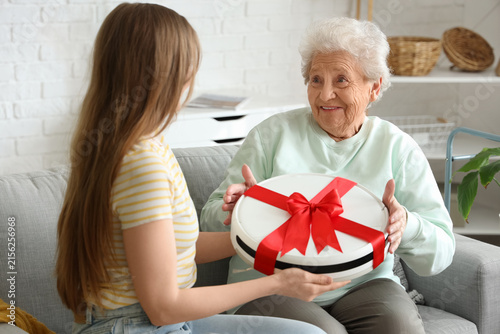 Young woman gifting robot vacuum cleaner to her grandmother at home