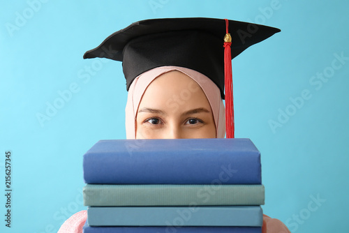 Female Muslim graduate with books on blue background