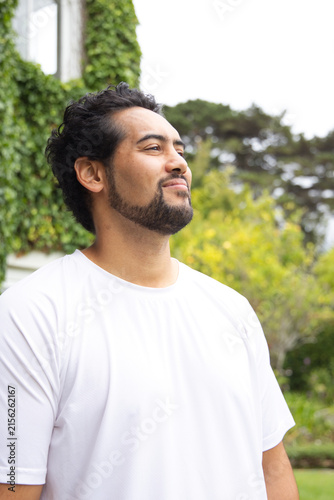 African American man in 30s standing, gazing upward near ivy wall and window wearing white tee