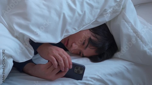 布団にもぐってスマホを見る男性