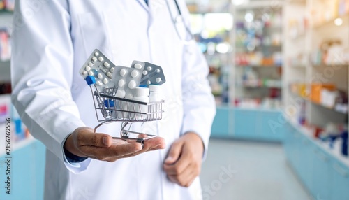 Pharmacist Hand Holding Miniature Shopping Cart with Blister Pack Medicines and Bottles in Pharmacy