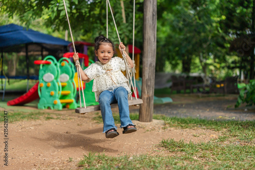 happy preschool child girl swinging on a wooden swing in a playground.