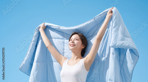 맑은 하늘 아래 하늘색 이불을 든 행복한 여성 · Happy Woman Lifting Light Blue Comforter Against Clear Sky