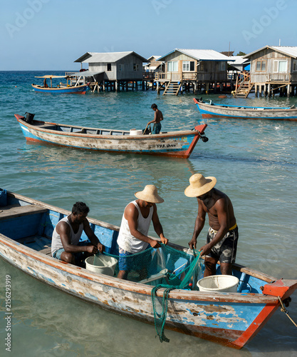 Authentic fishing village by the sea with colorful boats, local fishermen repairing nets, crystal-clear water, and bright summer light, realistic documentary travel photography